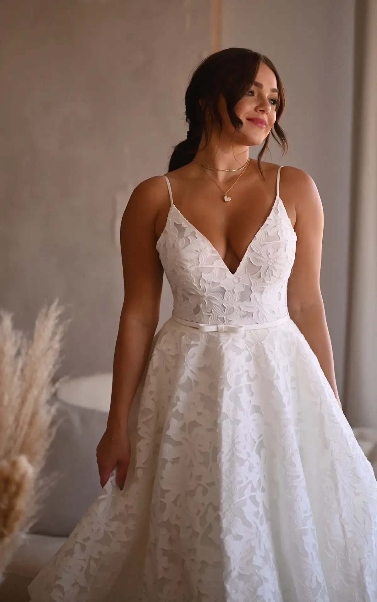 Model is wearing a classic A-line wedding gown featuring floral organza lace, a deep V-neckline, spaghetti straps, and hidden pockets.