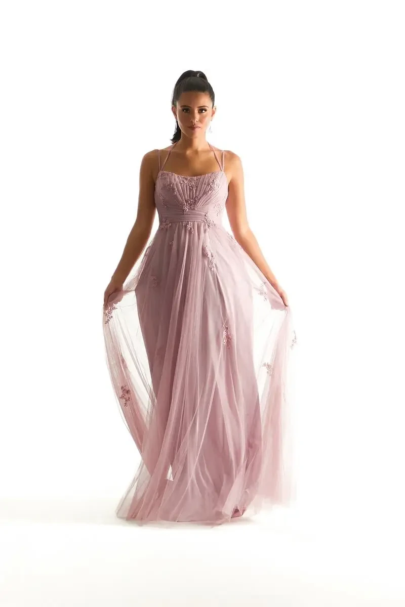Model is wearing a desert rose English Net bridesmaid dress with a pleated scoop neckline, floral appliqués, and double straps that tie at the back.