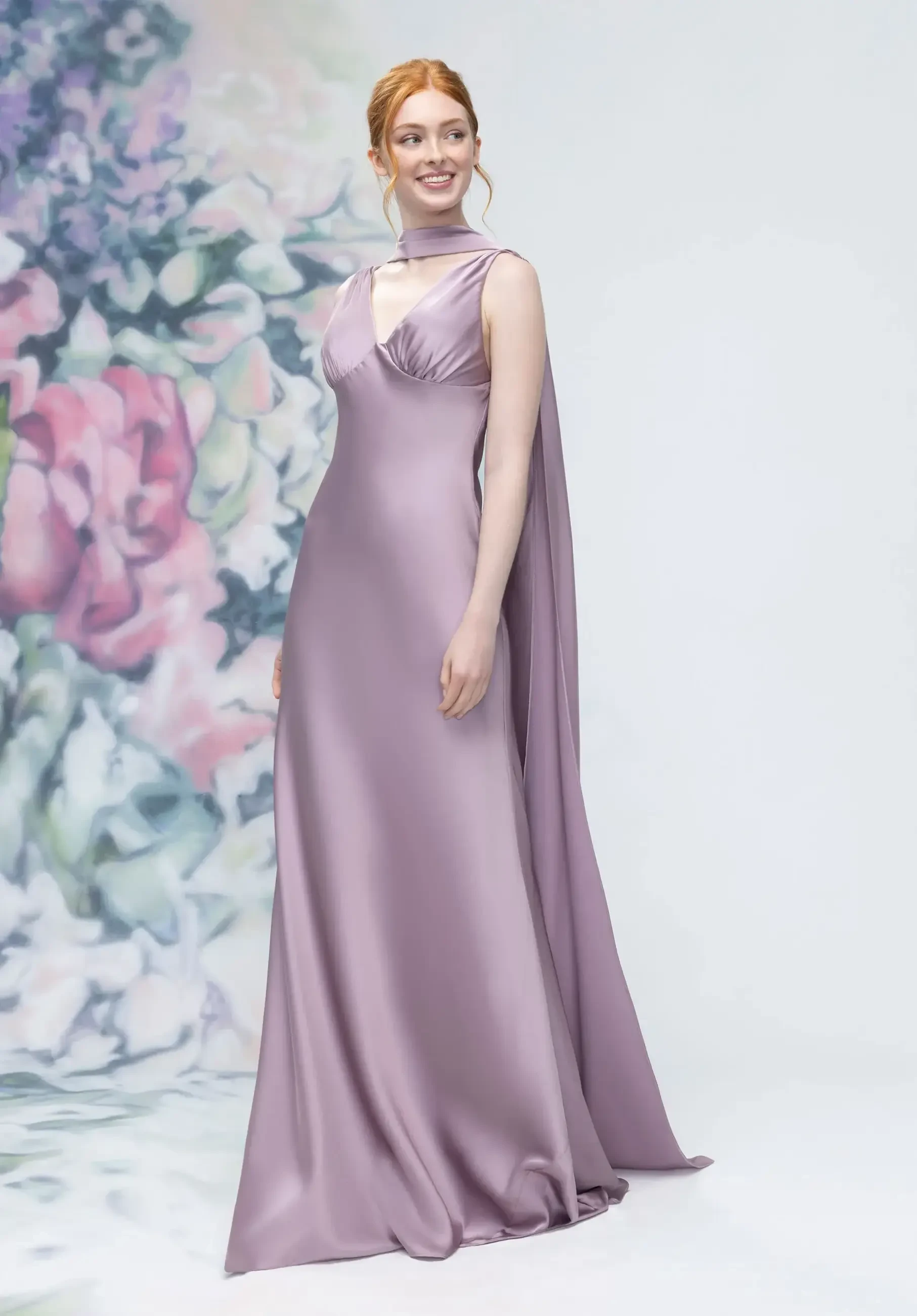A woman in a purple satin gown with a high neckline and flowing cape, posing against a floral background.