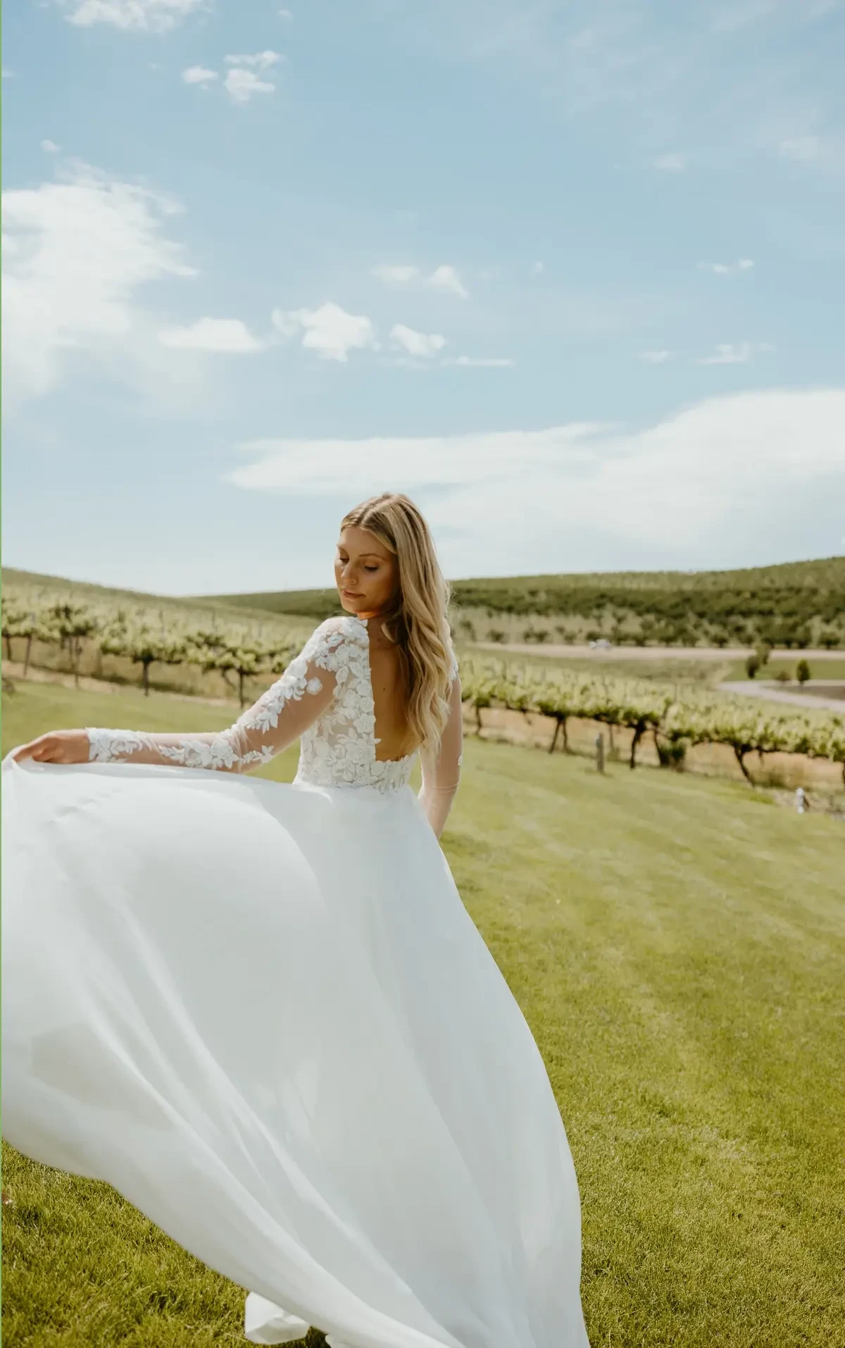 Model is wearing a romantic A-line gown with a floral lace bodice, chiffon skirt, plunging neckline, and optional sheer long sleeves.