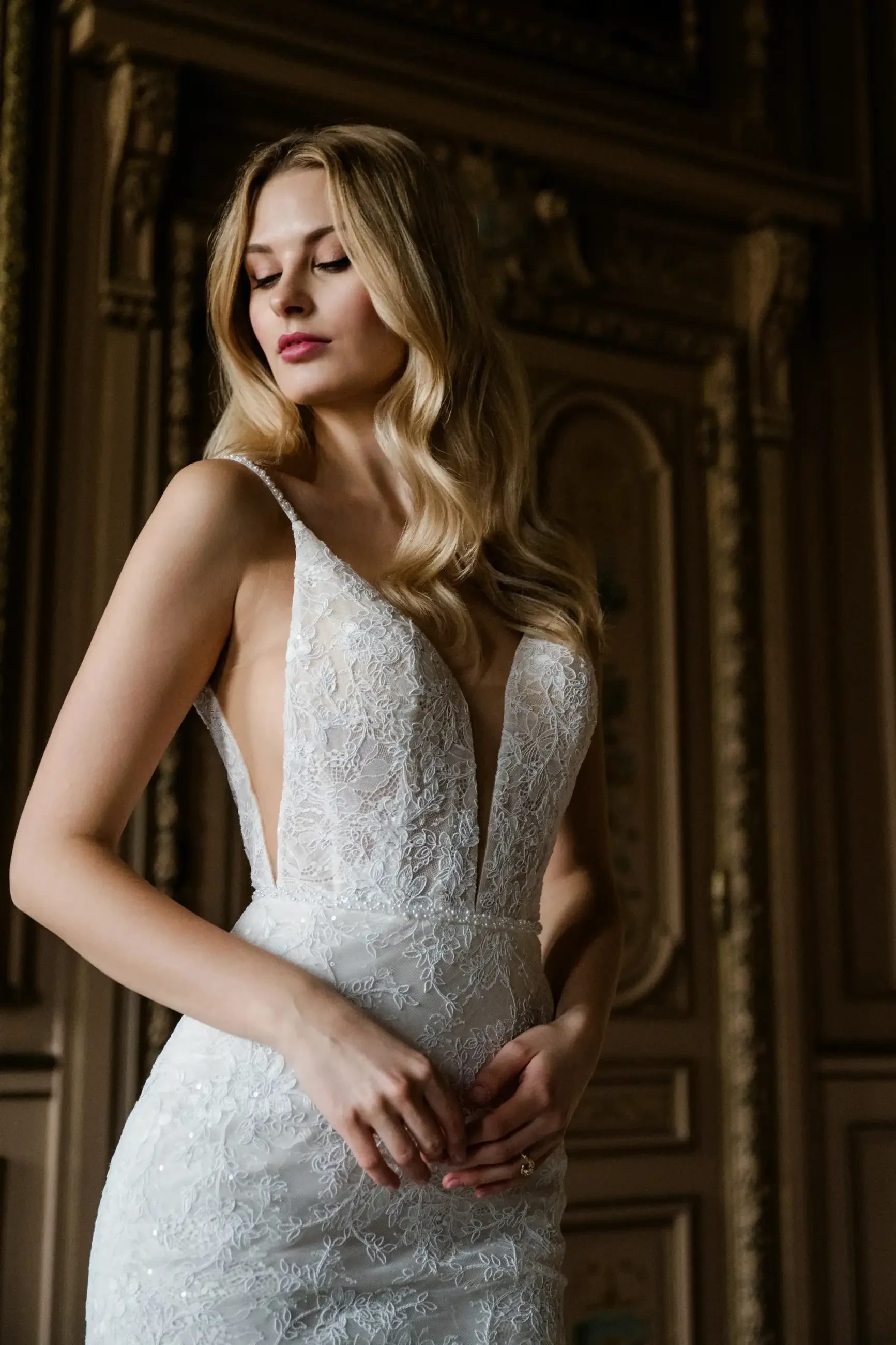 A woman wearing an elegant wedding dress with a deep neckline, standing gracefully in a decorative indoor setting.