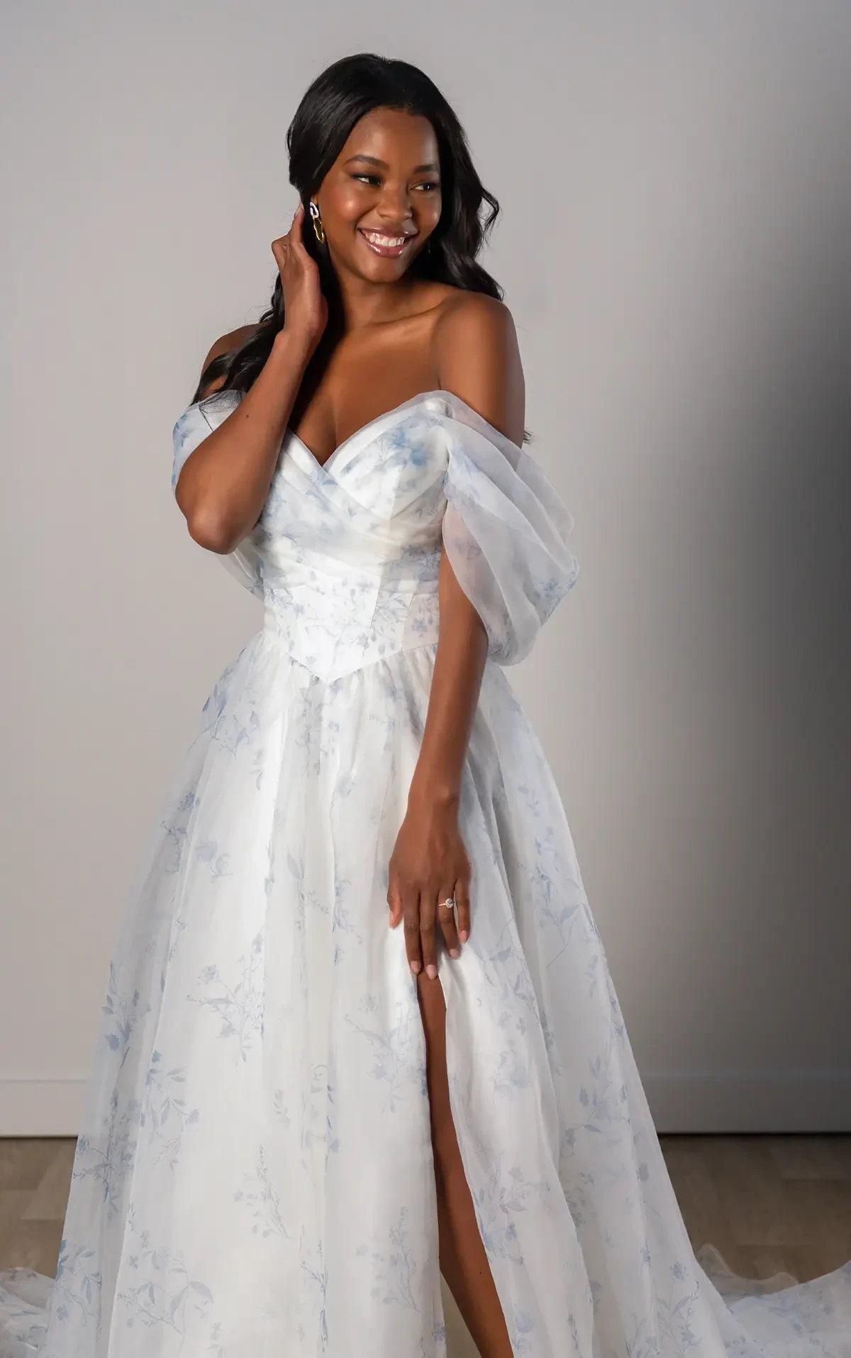 Model is wearing an organza off the shoulder a-line wedding dress with blue floral prints