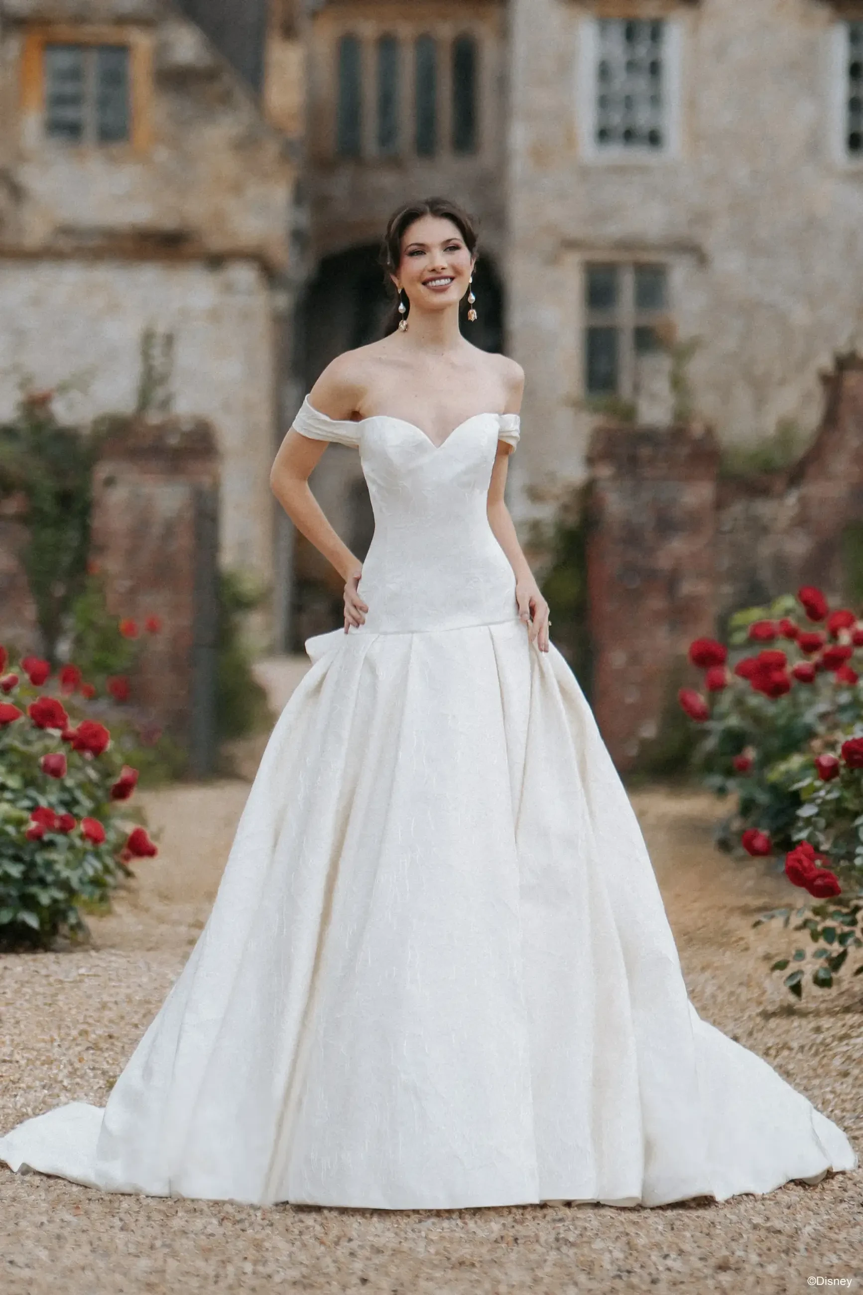 A woman wearing an elegant white wedding dress, posing outdoors with roses in the background.