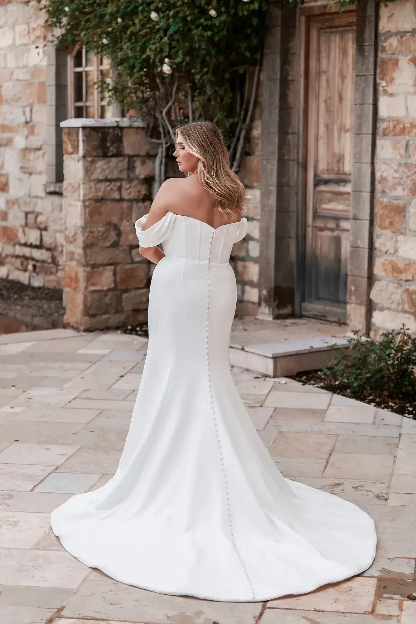 Model is wearing a plus size off the shoulder wedding dress with a cowl neckline by allure bridals