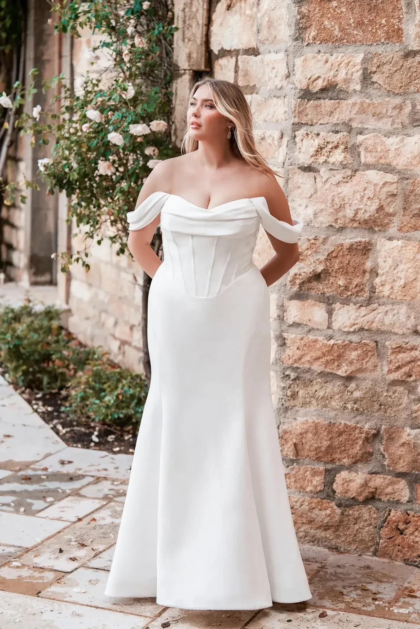 Model is wearing a plus size off the shoulder wedding dress with a cowl neckline by allure bridals