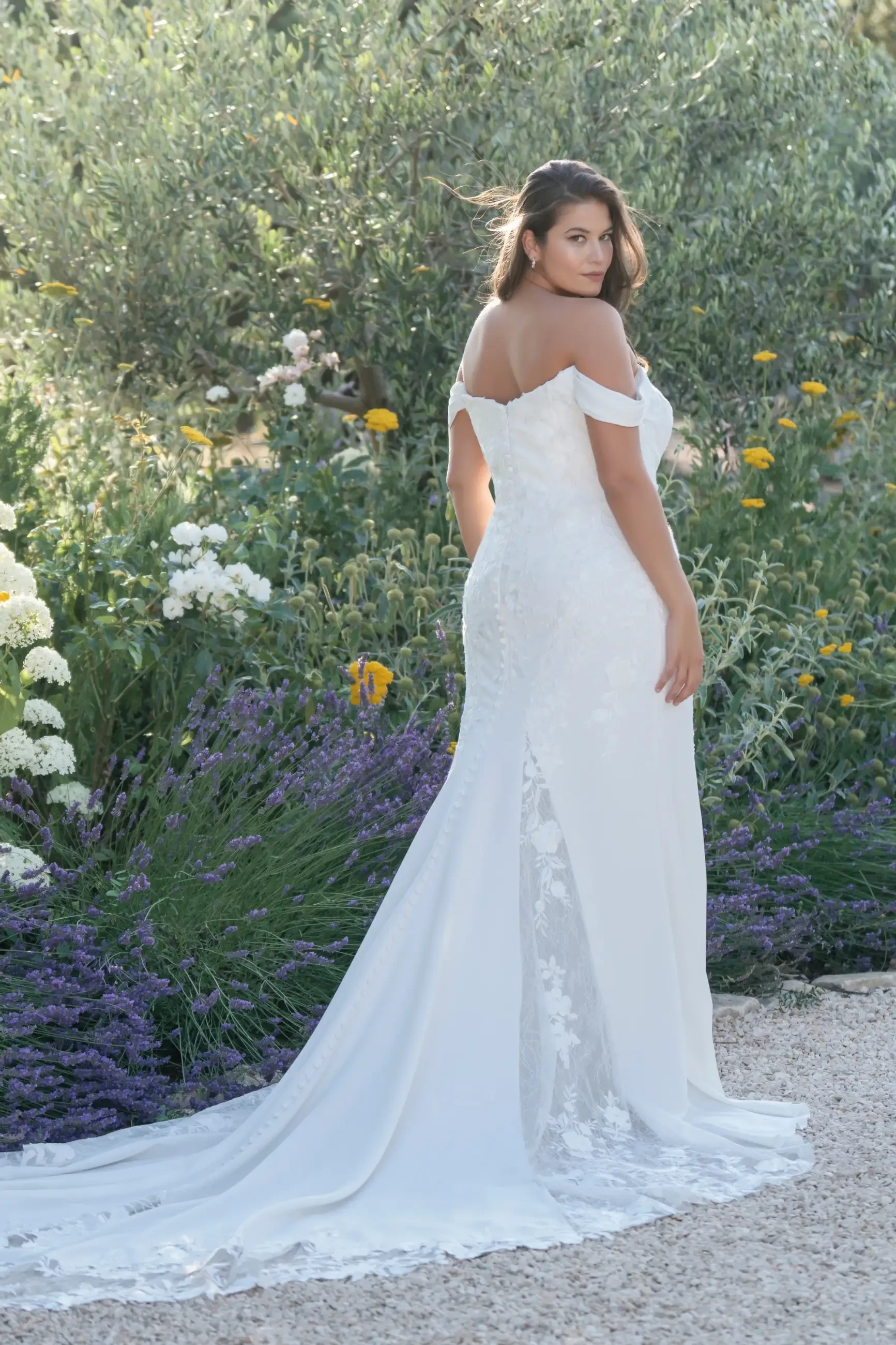 Model is wearing a plus size off the shoulder crepe sheath bridal gown with lace paneling by allure bridals